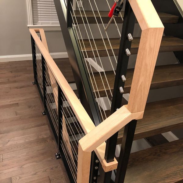 A close-up of a wooden staircase handrail transitioning from a horizontal landing to a downward slope on black metal posts.