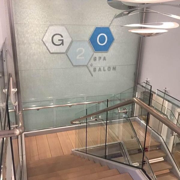 A staircase leading down to a G2O Spa + Salon entrance with a logo on a glass wall and a modern light fixture overhead.