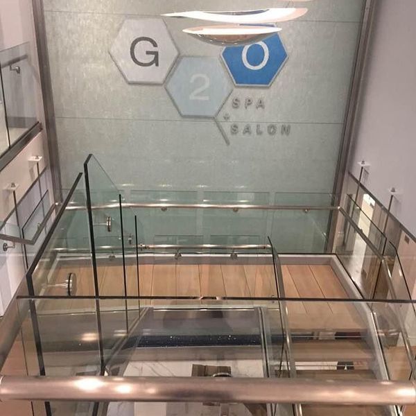 A high-angle view looking down a modern staircase with glass railings toward a G20 Spa & Salon sign on a textured wall.