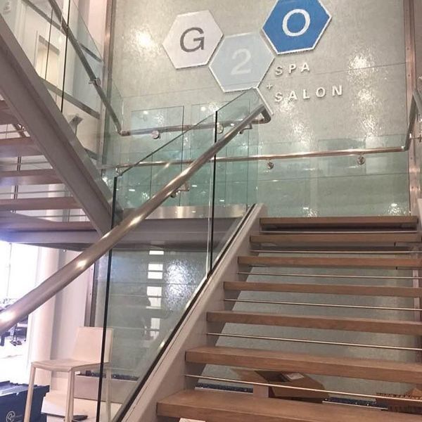 Stairs with glass railings lead to a wall featuring a G20 Spa & Salon logo in hexagon shapes.
