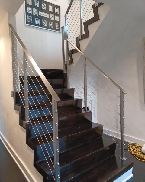 Modern staircase featuring dark wooden steps, stainless steel posts, and cable railings, leading to an upper landing.