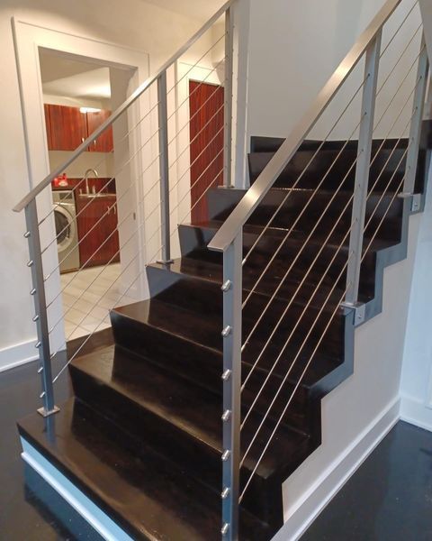 Dark wooden staircase with a sleek silver cable railing and metal posts, leading to an adjacent room with a laundry area.