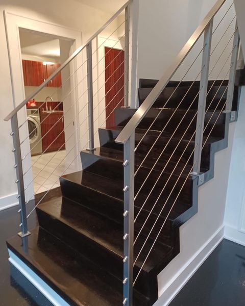 A staircase with dark wood steps and a modern metal railing featuring horizontal tensioned steel cables.
