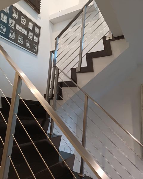 A modern staircase with dark steps, white walls, and a silver metal railing with thin horizontal cable infills.