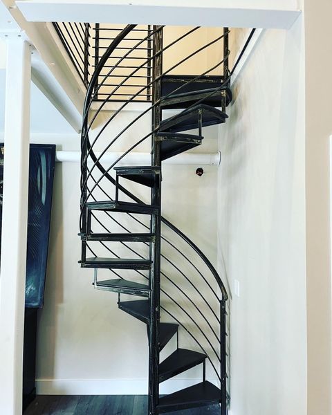 A black metal spiral staircase ascends from a wood floor to a loft space in an interior room.