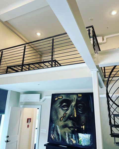 A lofted room with metal railings overlooks a living area featuring a large, artistic portrait of Benjamin Franklin.
