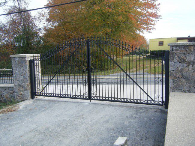 Black metal driveway gate between stone pillars, closed at the entrance to a property