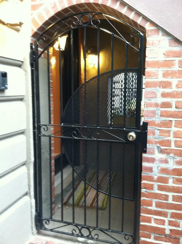 Black metal gate at a brick-arched doorway, with a lit entryway behind it.