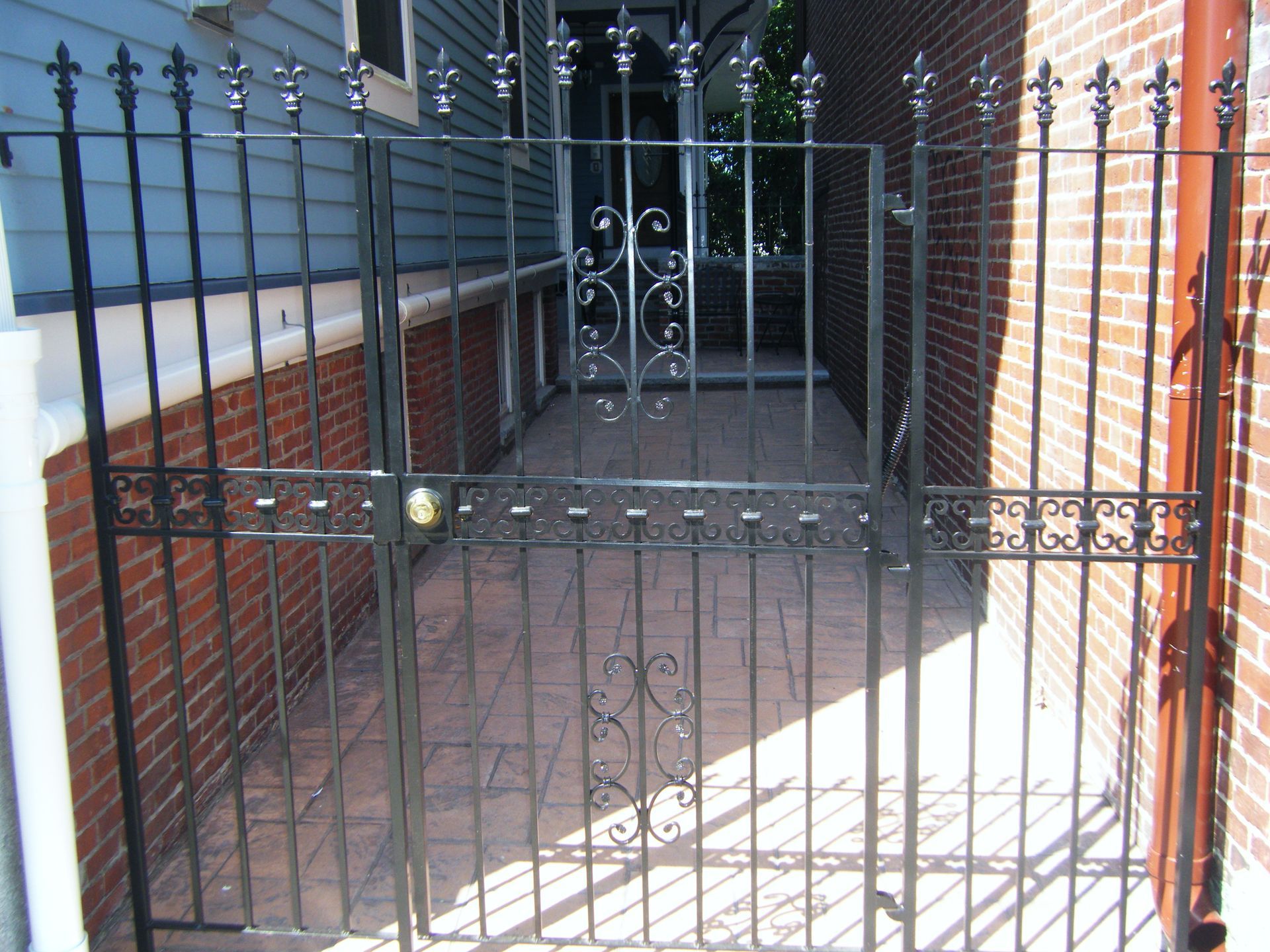 Black metal gate blocking a brick walkway beside a brick building and iron fence
