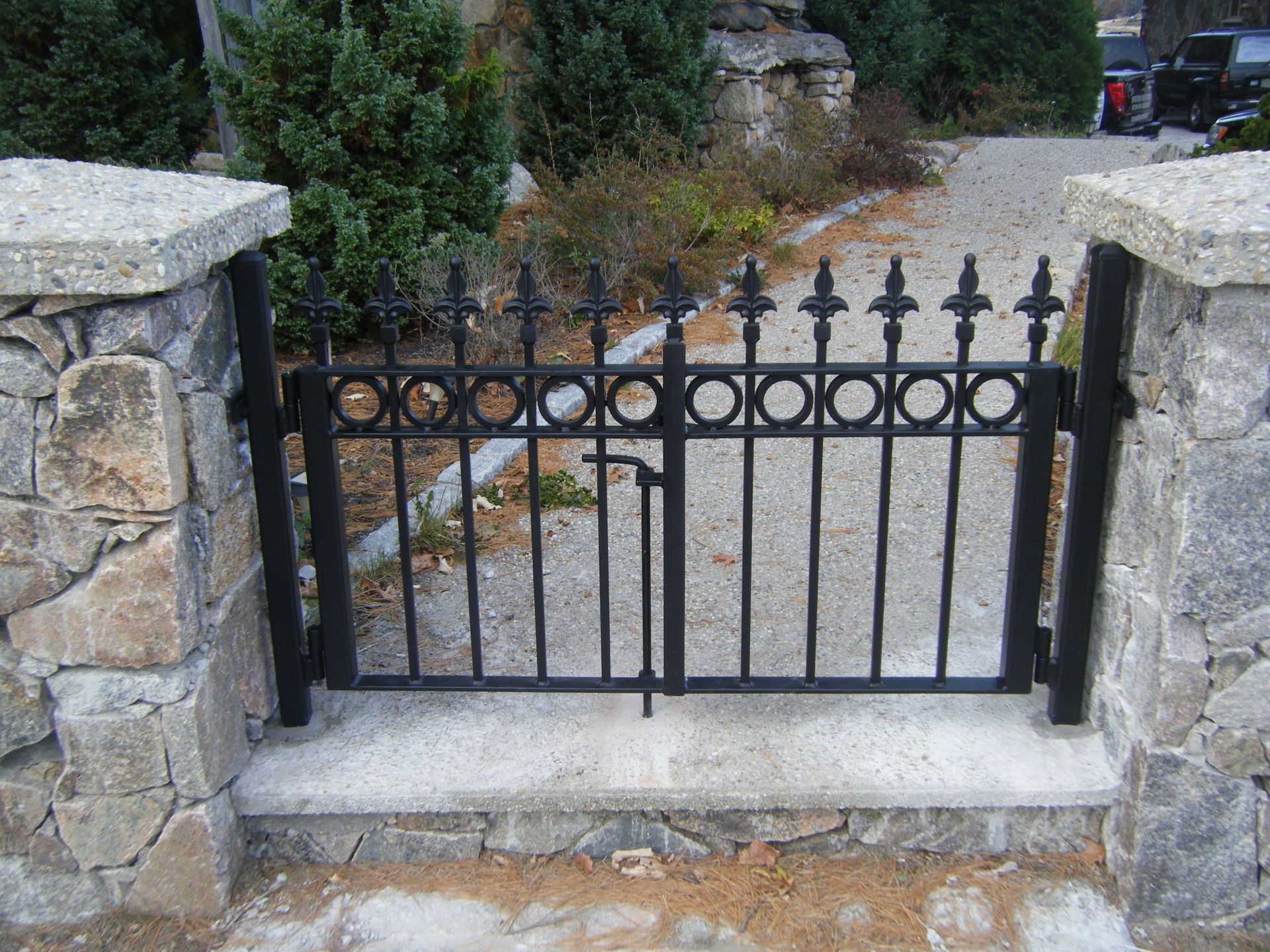 Black wrought-iron gate between stone pillars blocking a gravel driveway