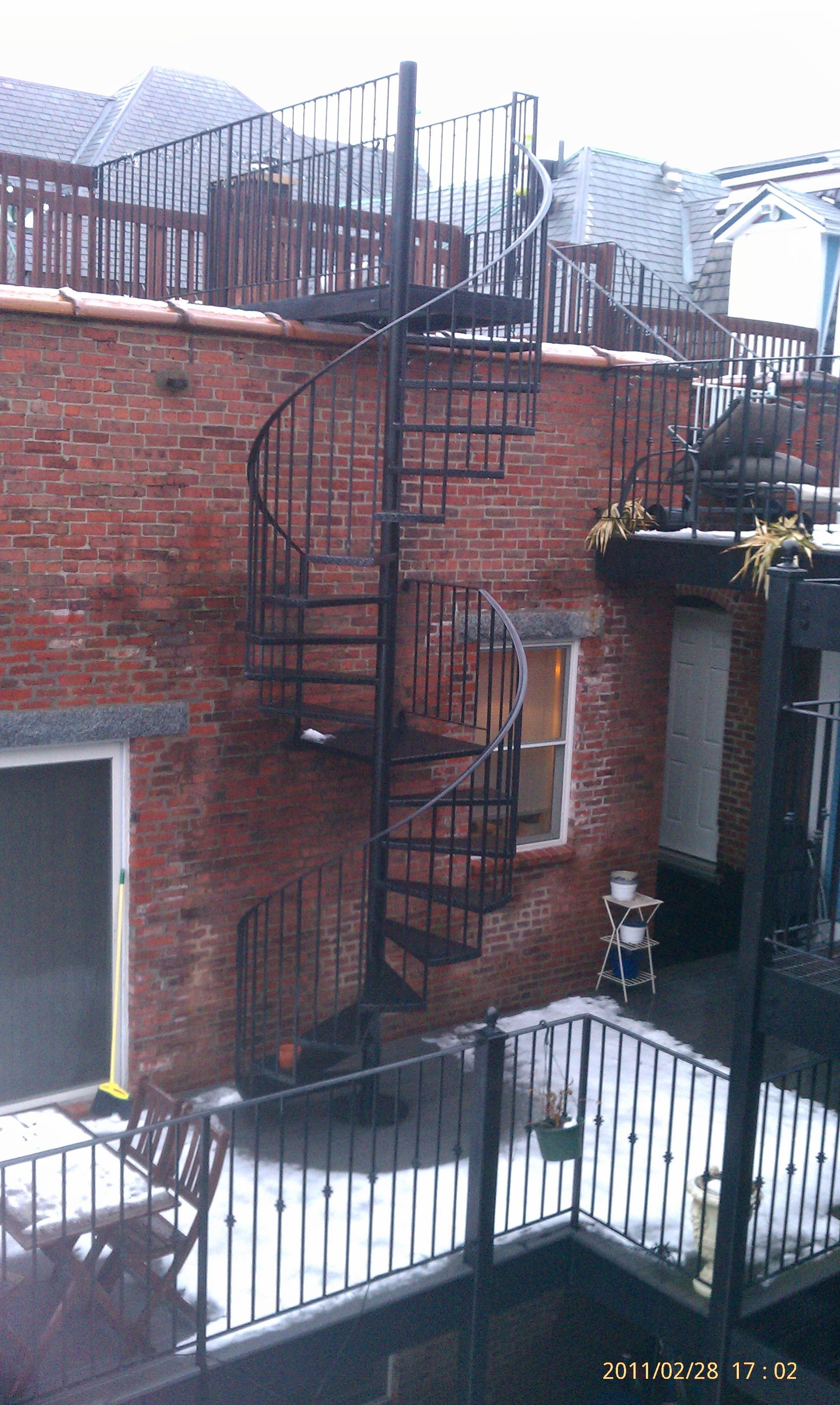 Brick building with black spiral fire escape and metal railings in a snowy courtyard