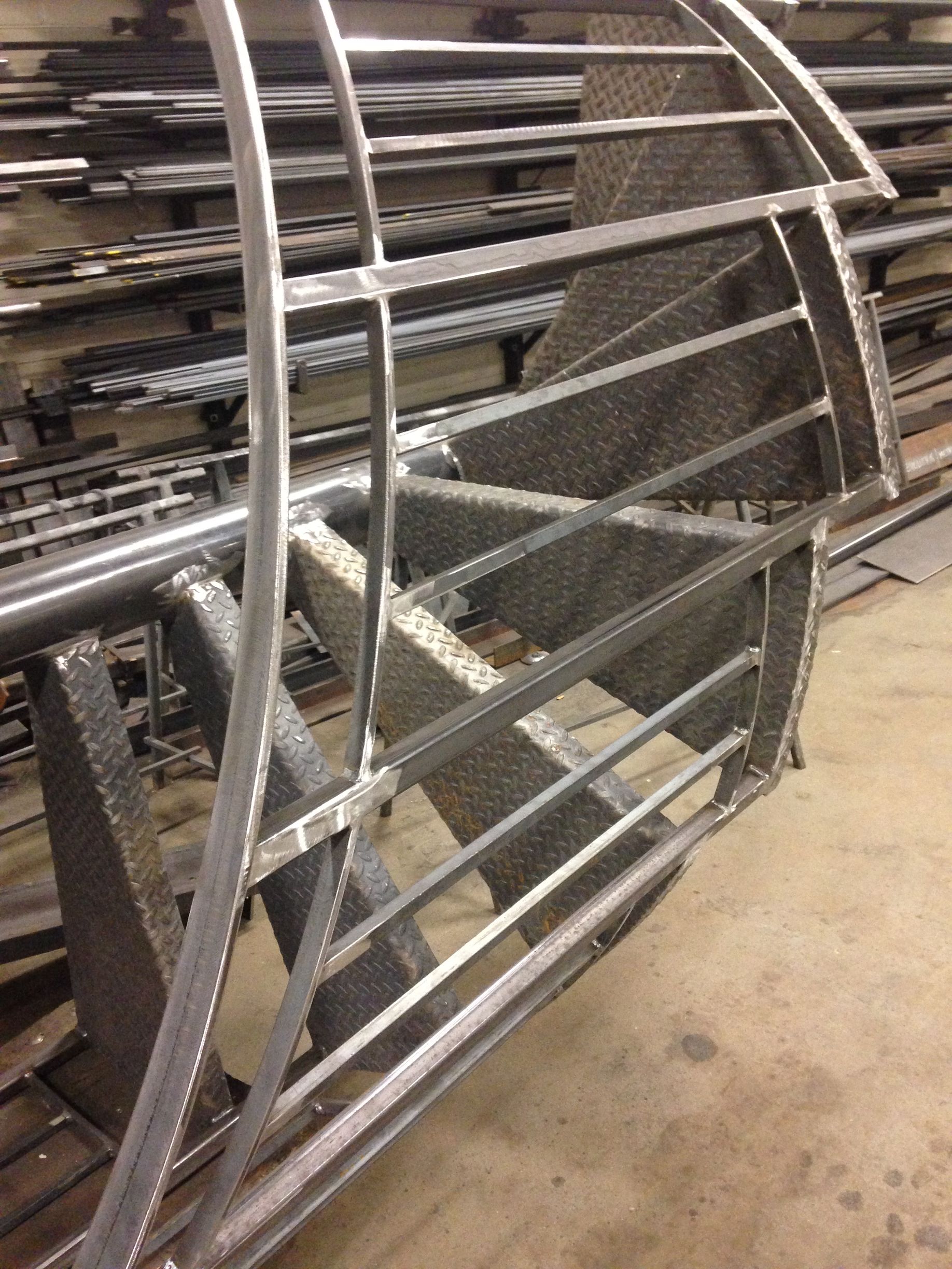 Stacked metal gate panels in a workshop or warehouse, with curved bars and horizontal slats.