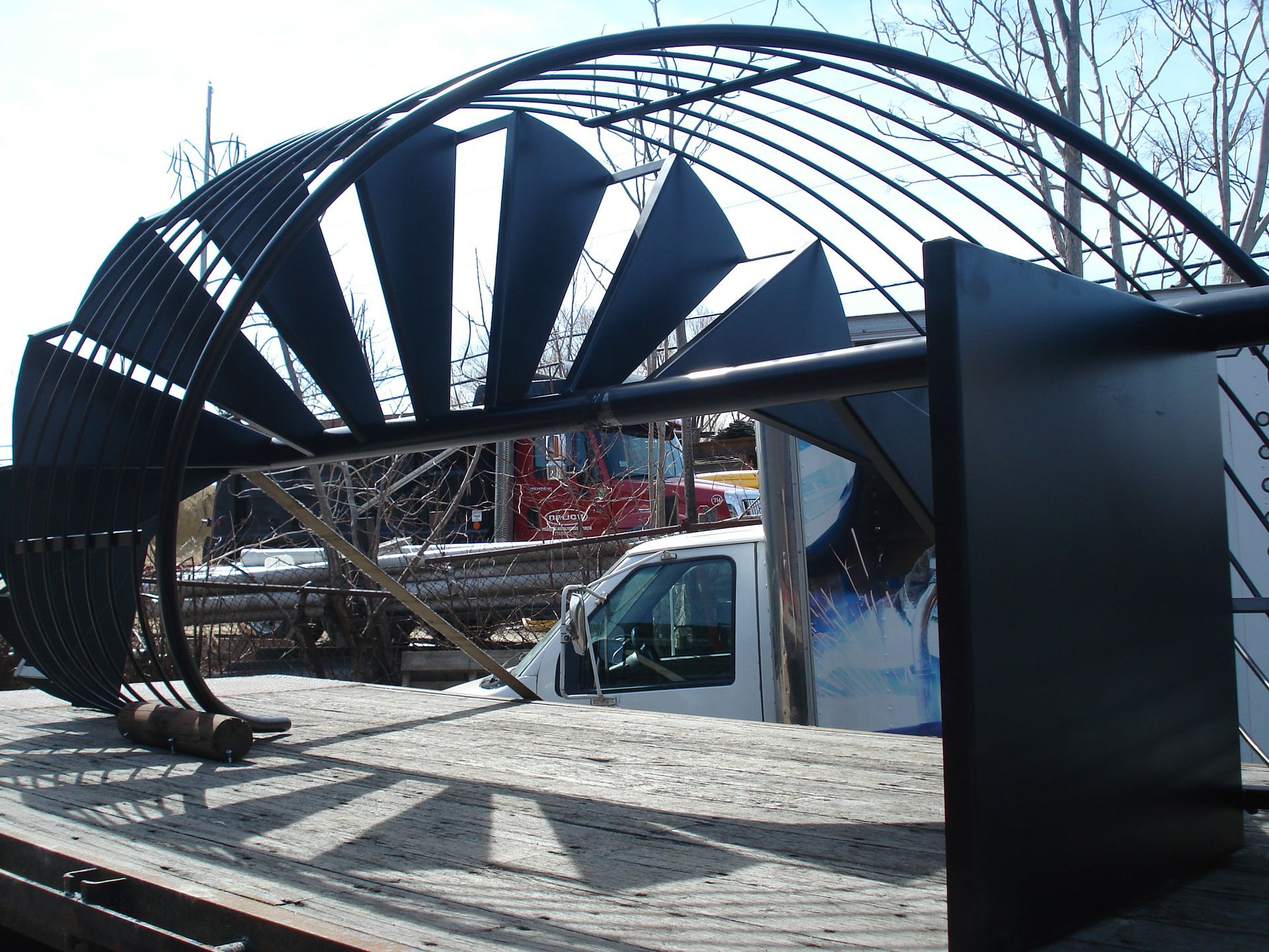 Large black metal sculpture with curved arches over a white van in an outdoor lot