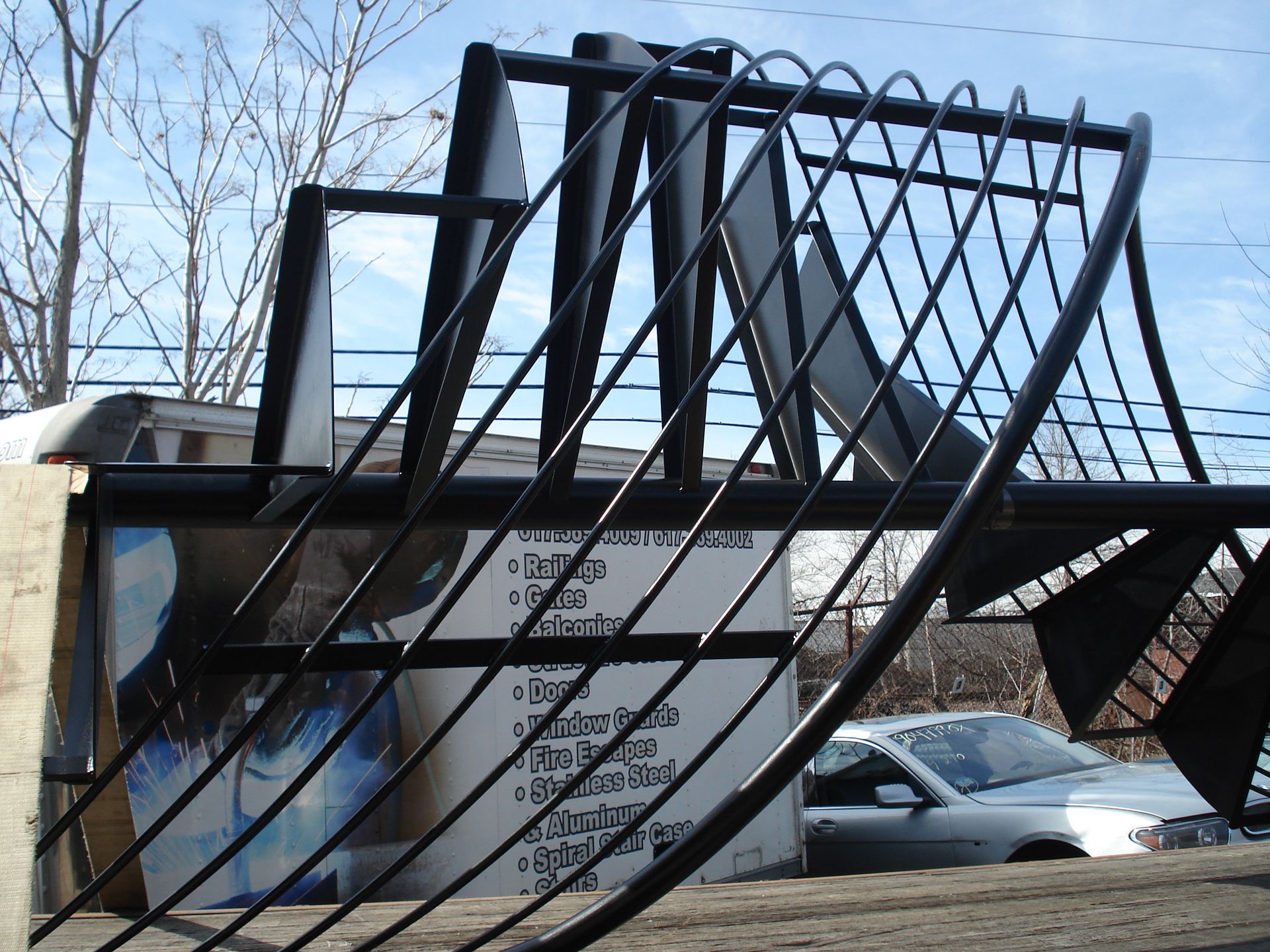 Large black metal sculpture shaped like a looping ribbon in an outdoor parking lot, with a car behind it.