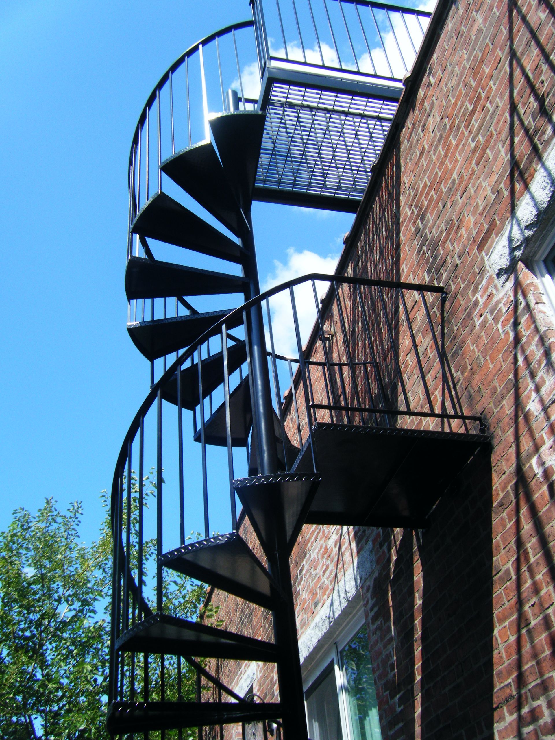 Black spiral metal staircase beside a brick building under a clear blue sky