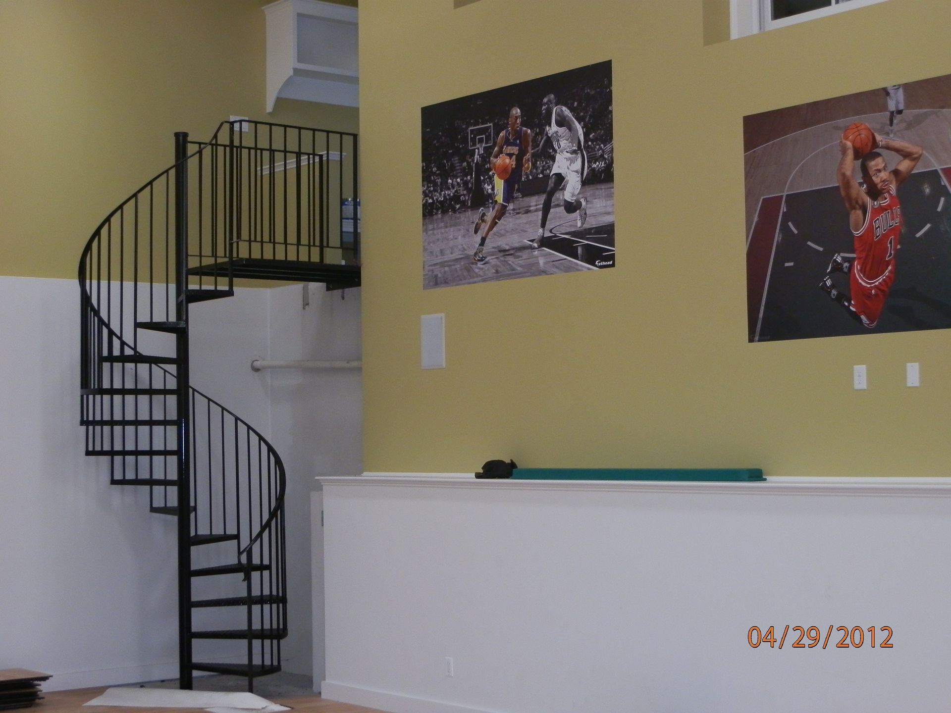 Interior room with black spiral staircase, beige walls, and two framed sports photos on the wall
