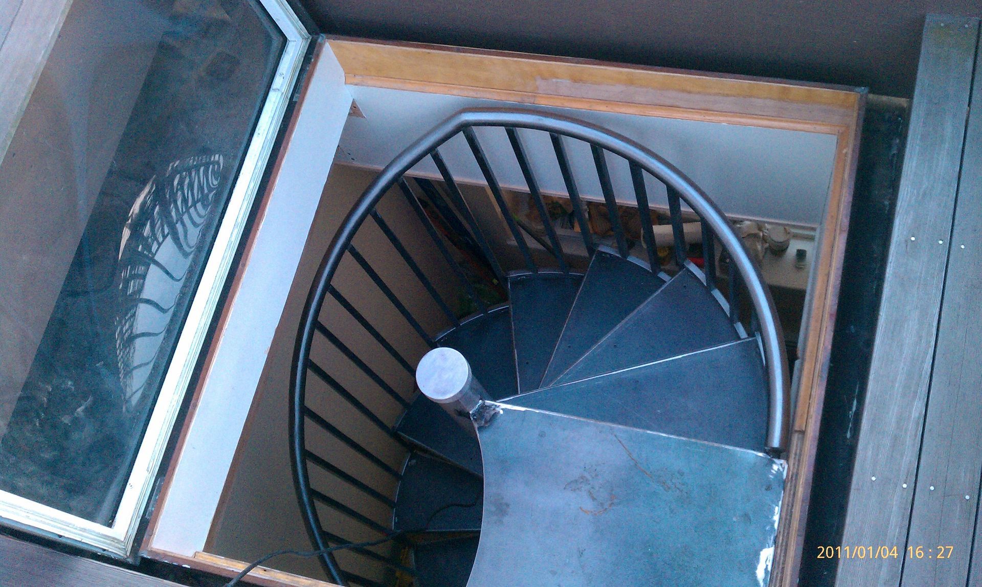 Top-down view of a spiral staircase inside a narrow shaft, with black railings and a white light fixture.