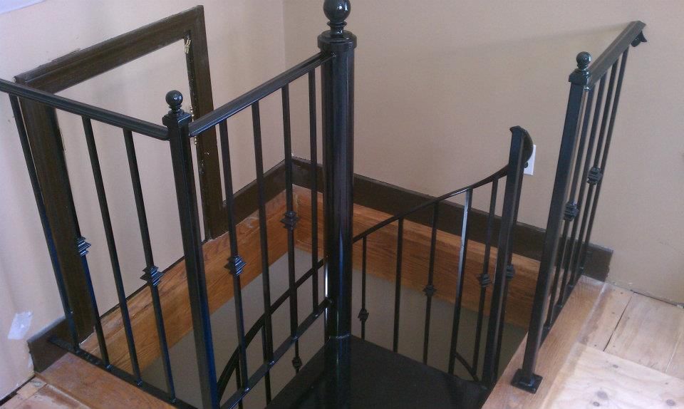 Black metal staircase with railings and wooden steps in a corner interior.