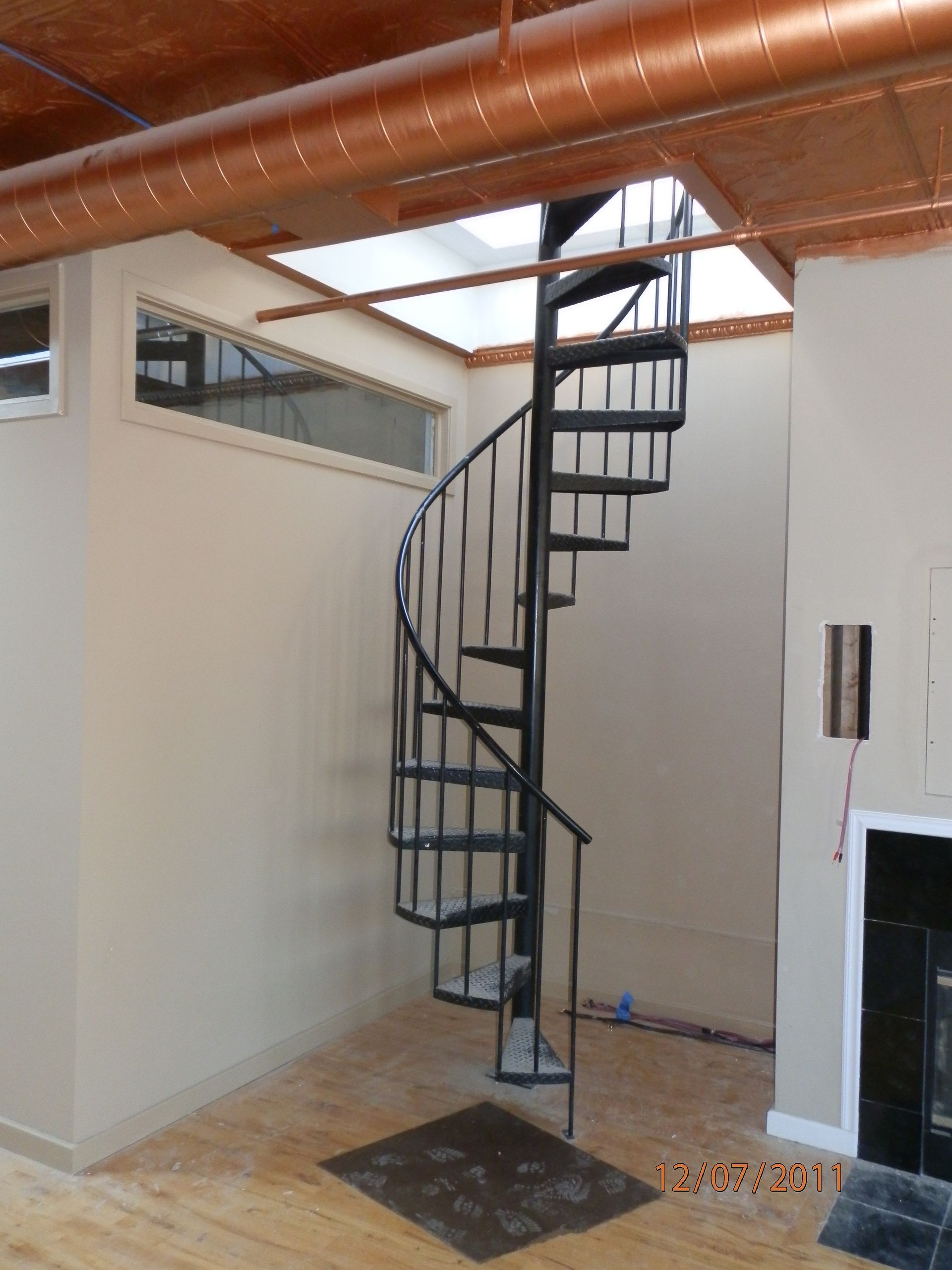 Spiral staircase in a room with wood floors, white walls, and exposed ceiling ducts