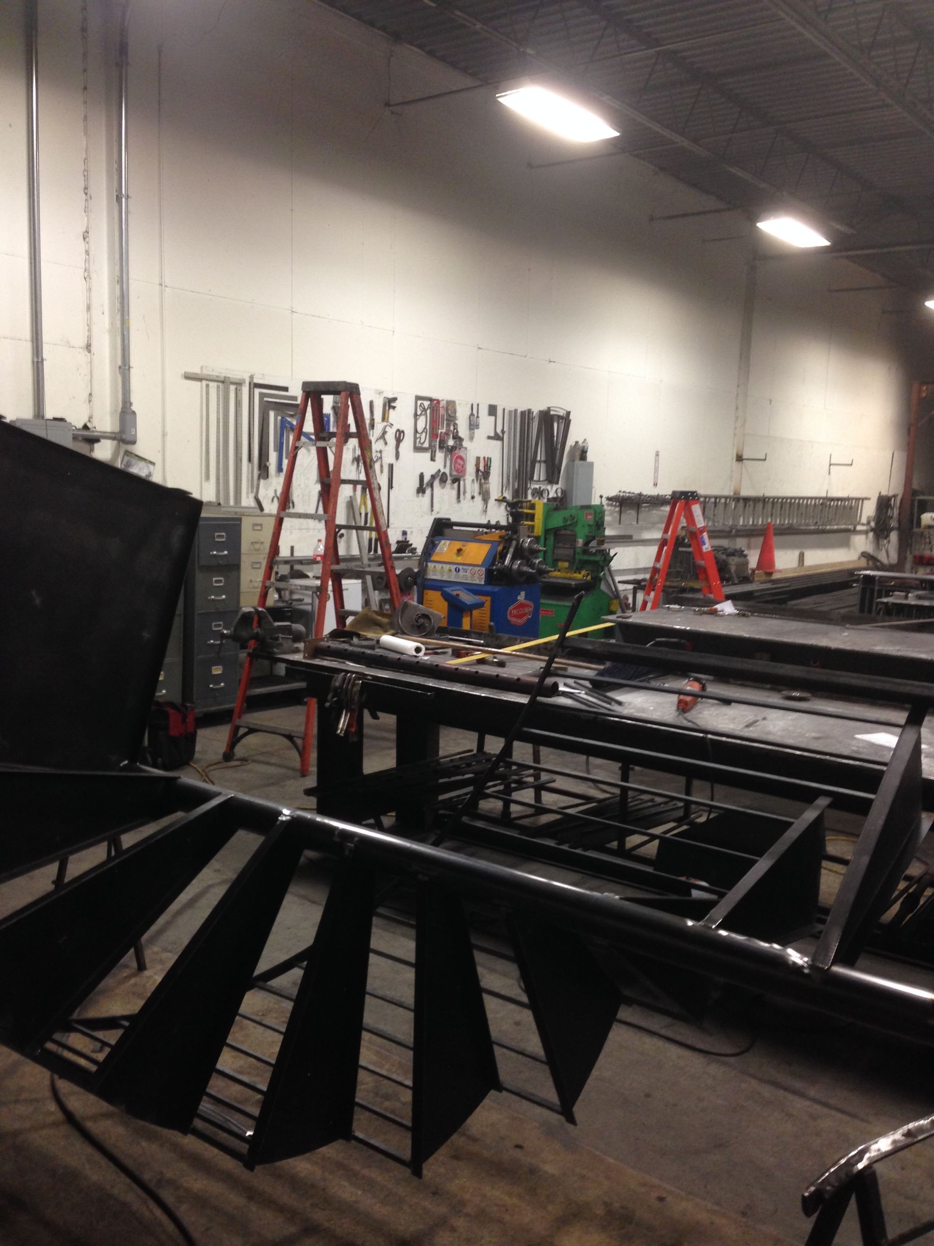 Industrial workshop with black metal frames, ladders, tools, and bright overhead lights
