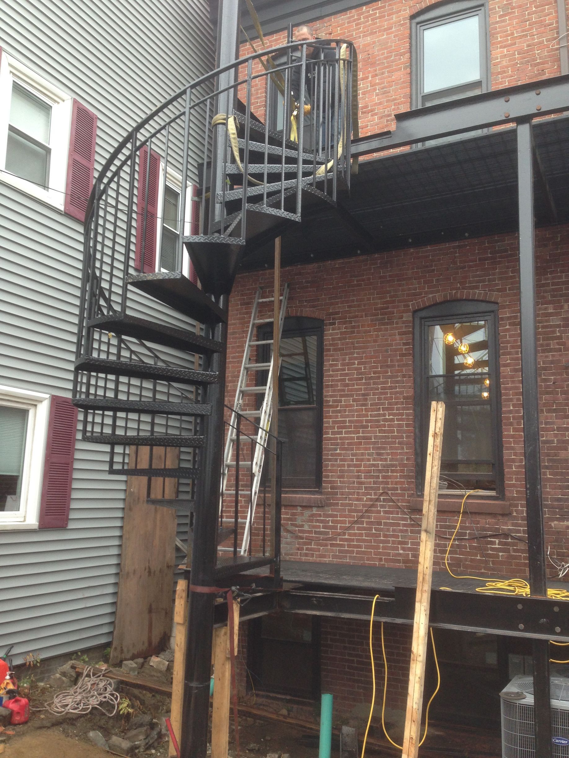 Narrow black metal fire escape on a brick building with an upper landing and stairs to a lower deck
