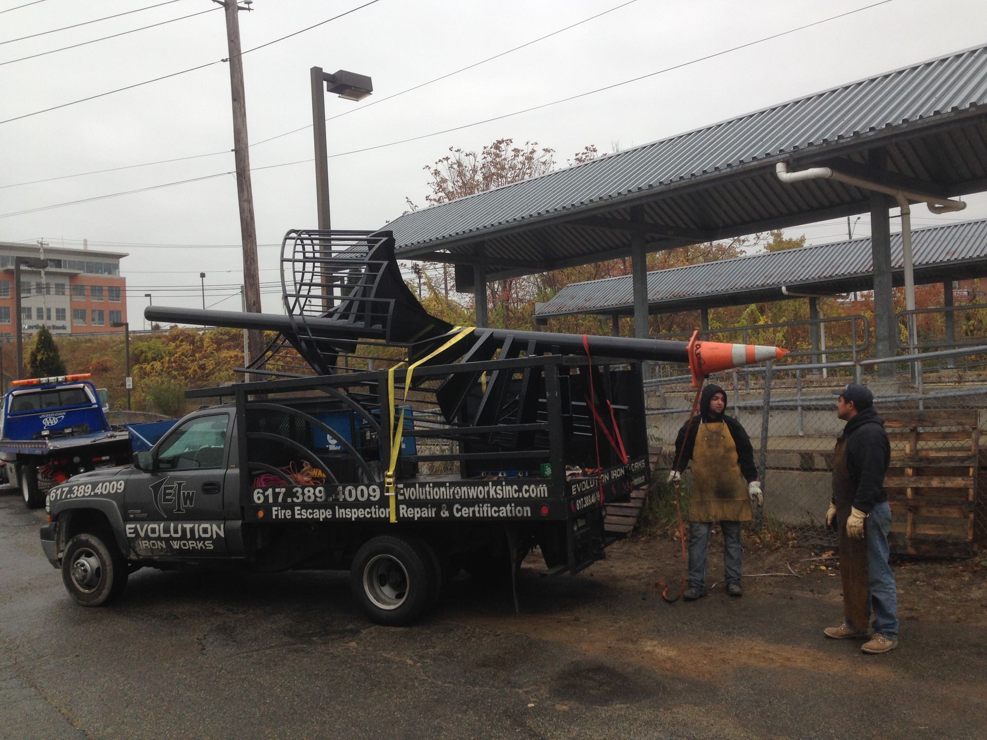 Pickup truck with roof rack and two workers on a rainy street beside a covered structure