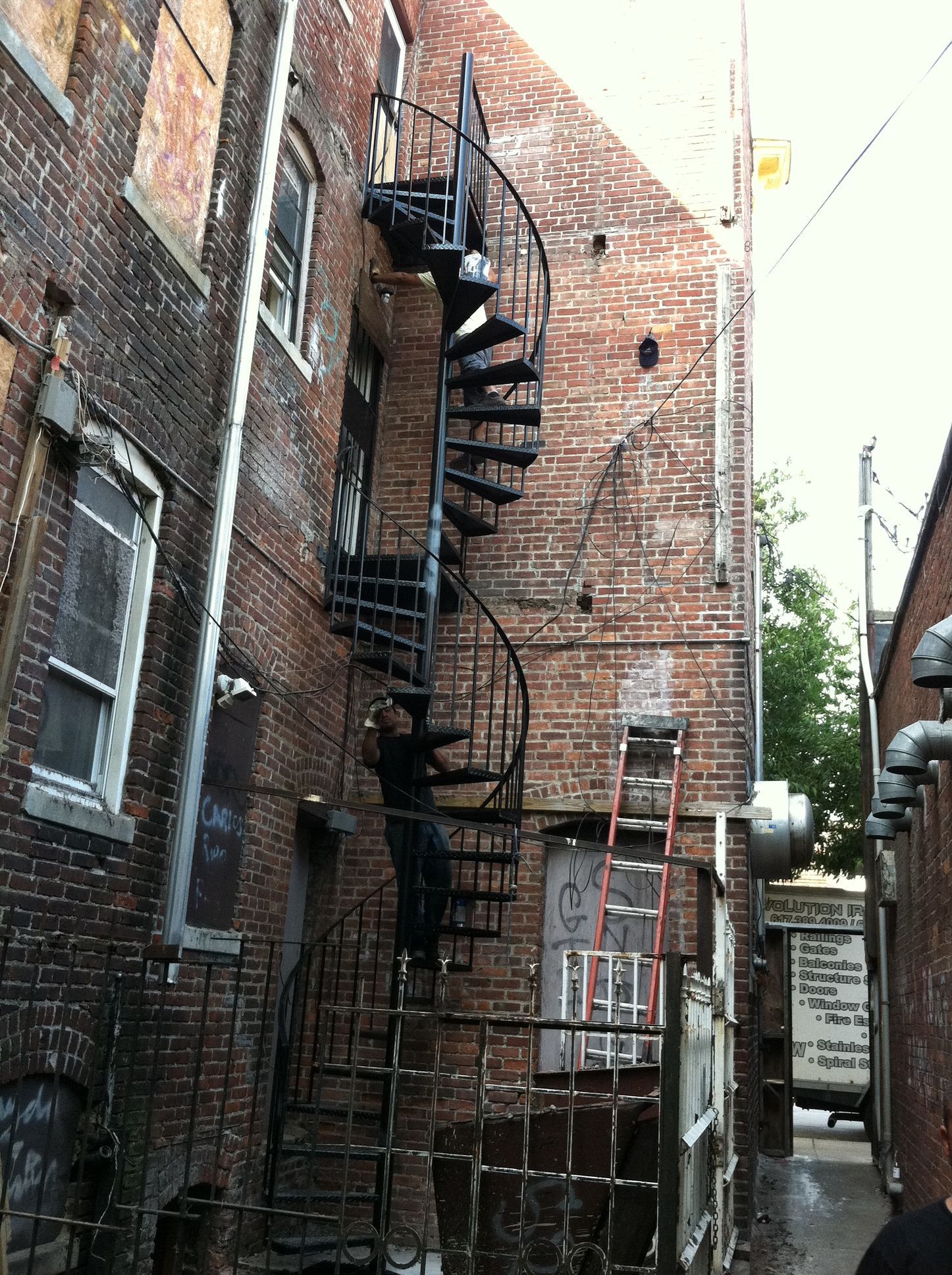 Narrow brick alley with black metal fire escape spiral staircase on building wall