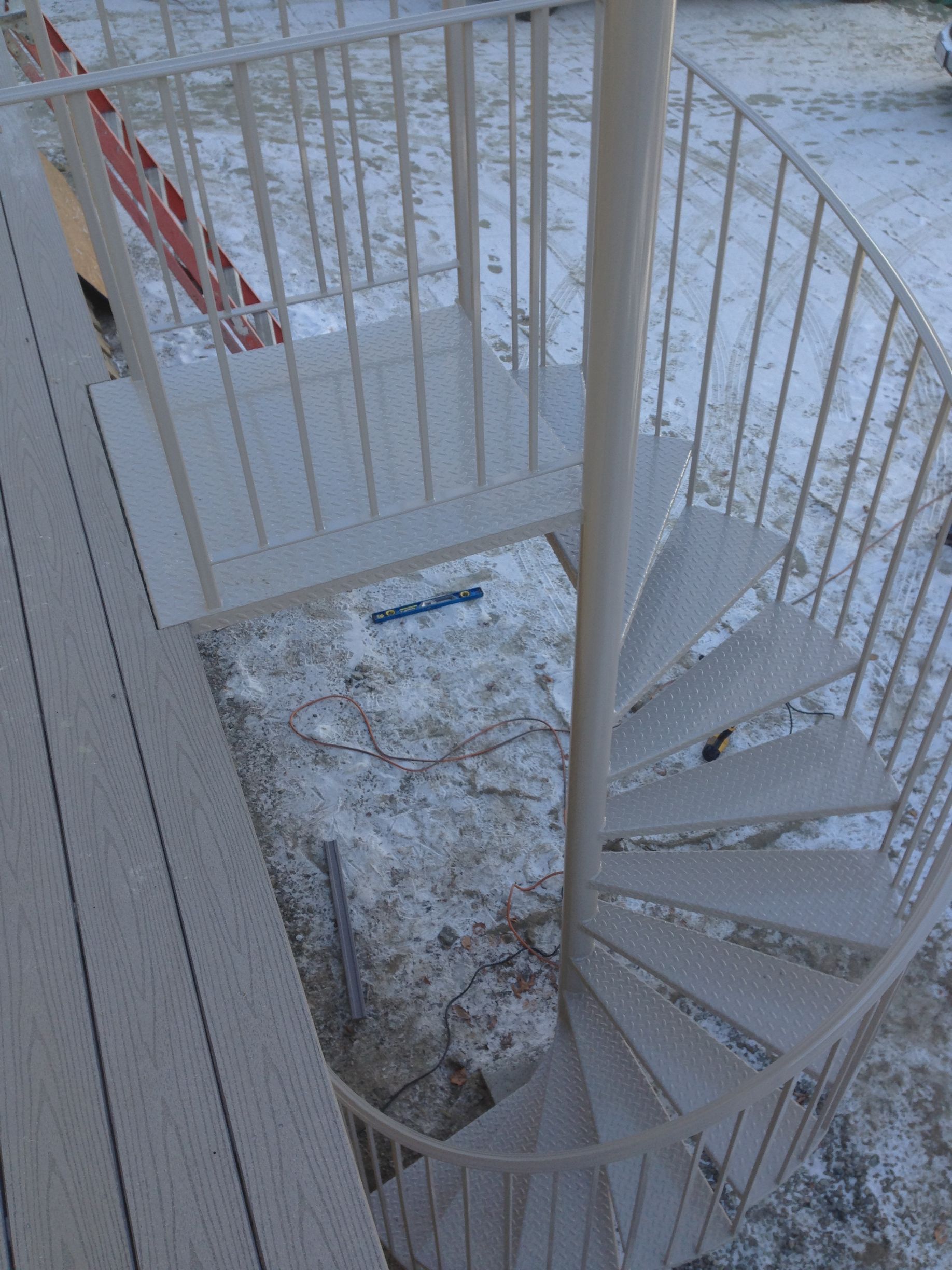 Snow-covered spiral staircase on a balcony beside white railings and a deck.