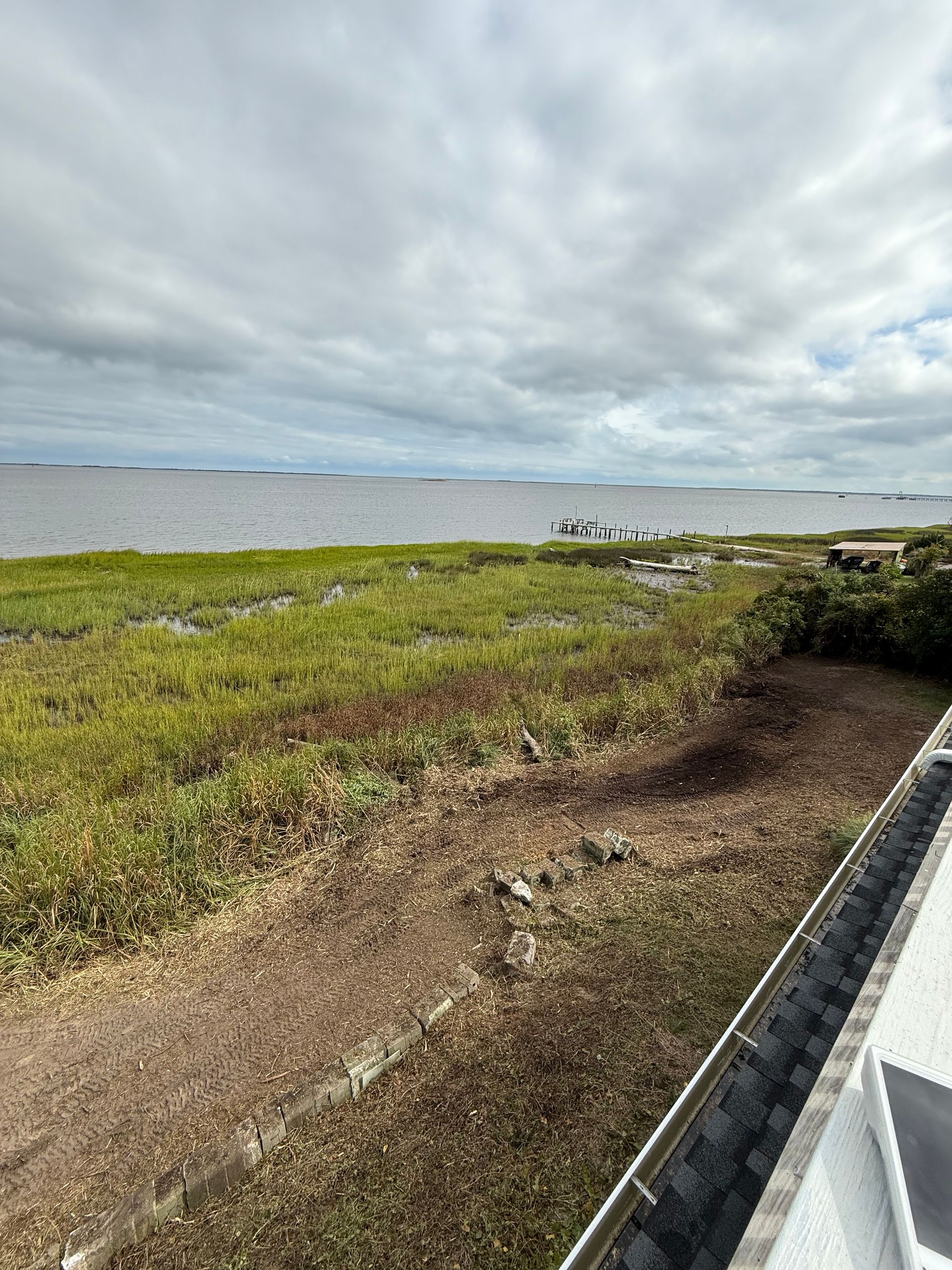 Grassy marsh leading to a wide body of water under a cloudy sky.