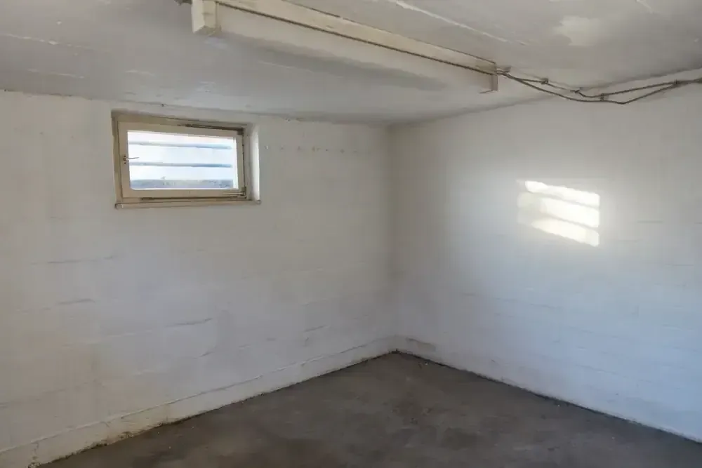 Empty basement room with white walls, small window, and concrete floor.