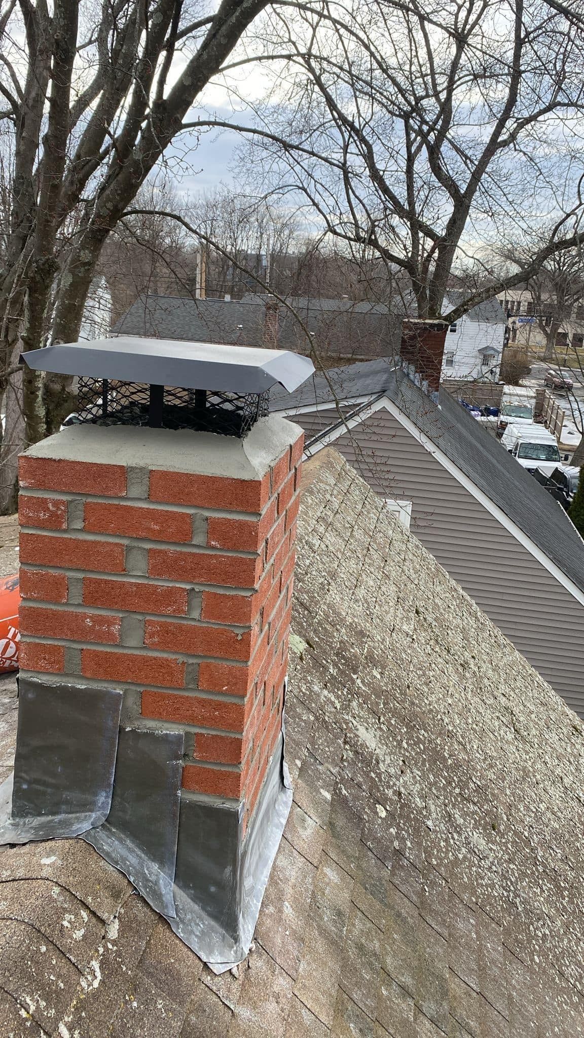 Brick chimney with a metal cap on a gray rooftop.