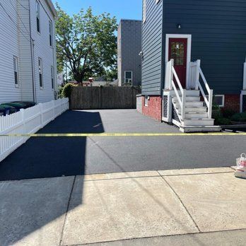 Newly paved driveway with white fence, steps to a red door, and a yellow caution tape.