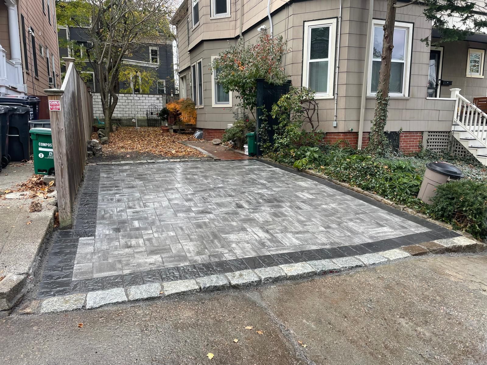 Paver driveway with a gray brick pattern, outlined by a dark border, next to a tan house.