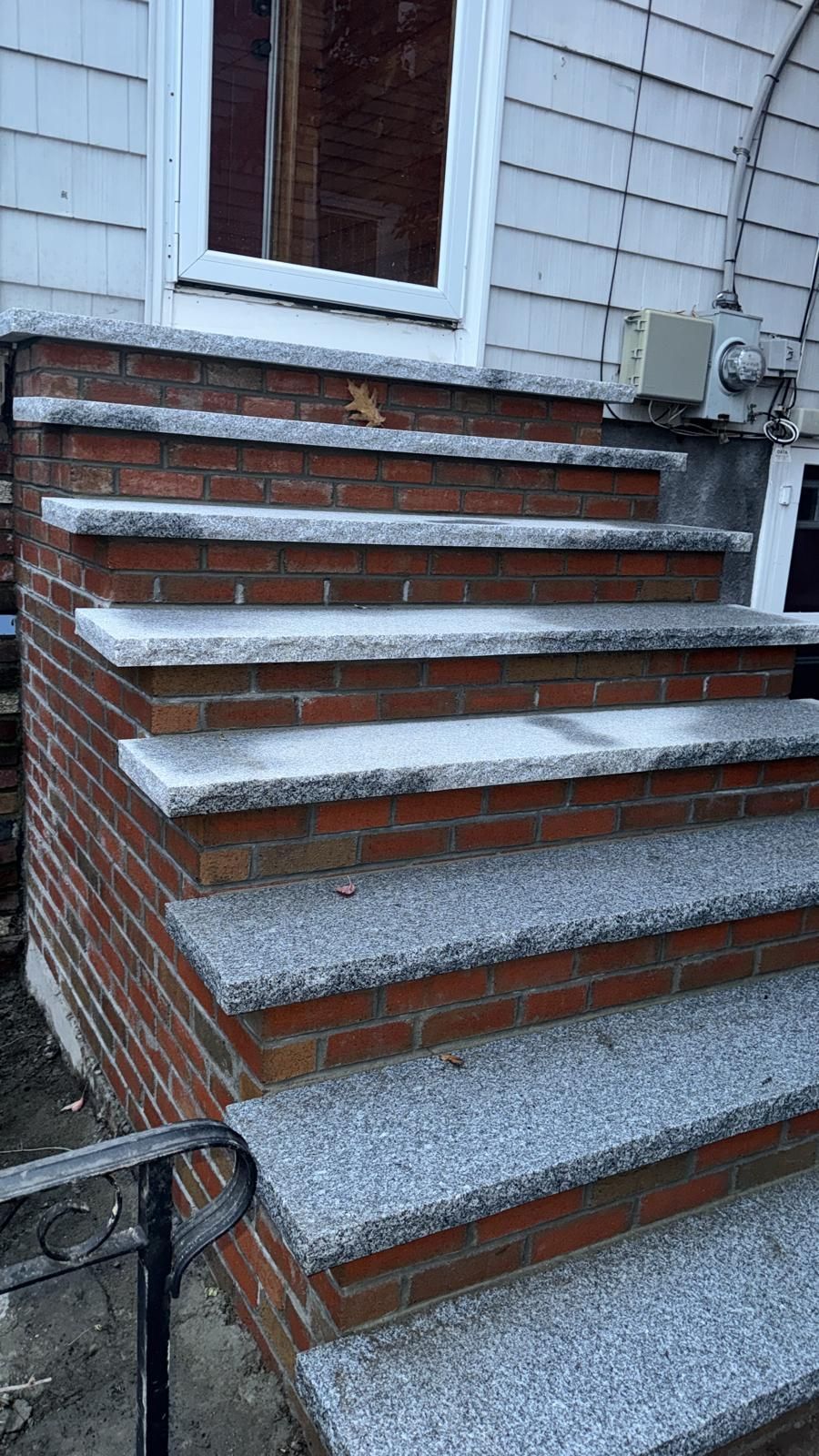 Brick and granite steps leading to a white door. The steps have a black metal railing.