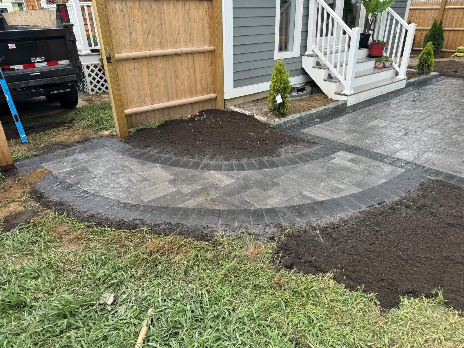 Newly constructed brick pathway, edged in dark gray, curves toward a light gray house entrance.
