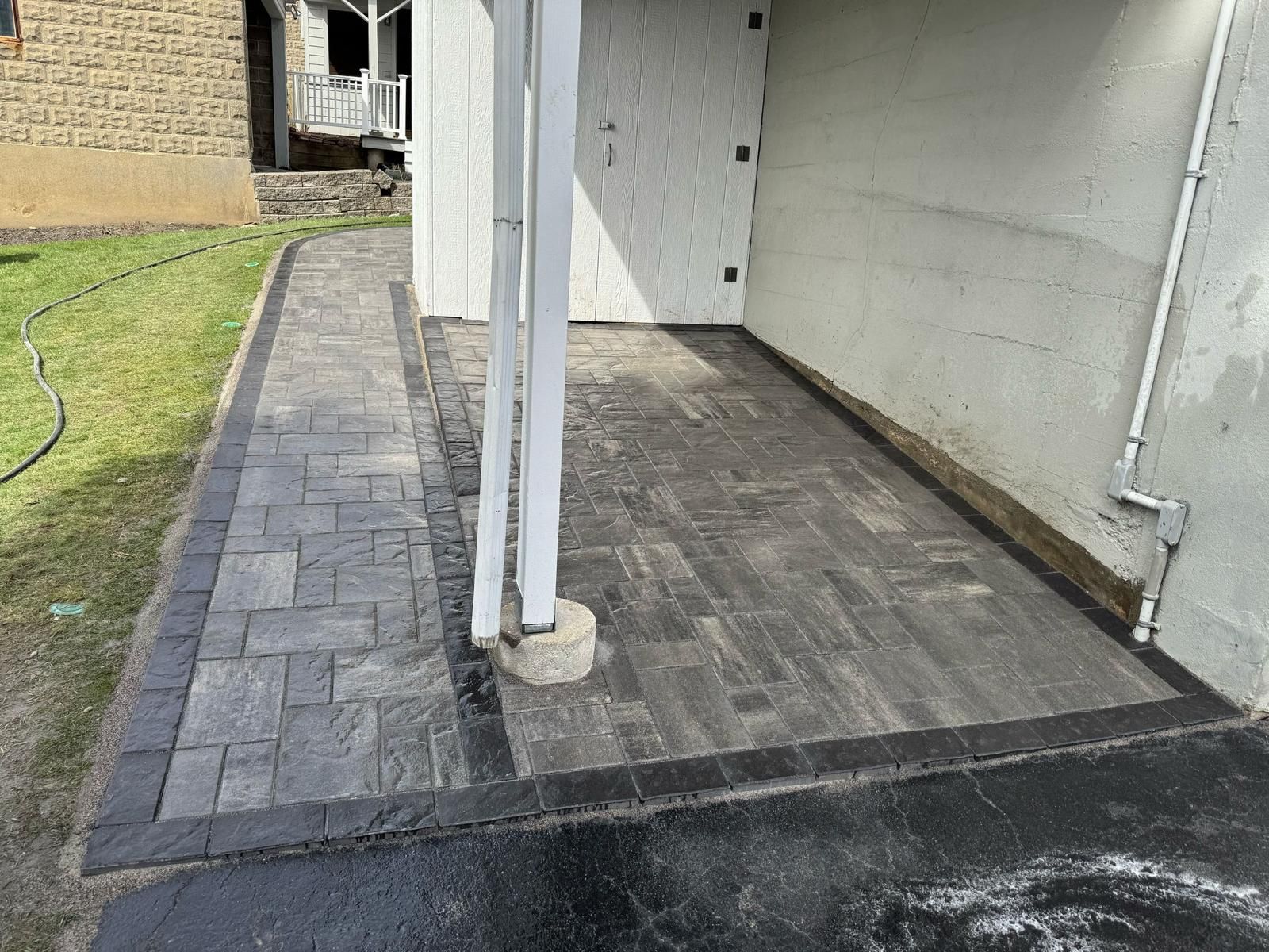 Patio with gray pavers, black border, white support post, concrete walls, next to a building.