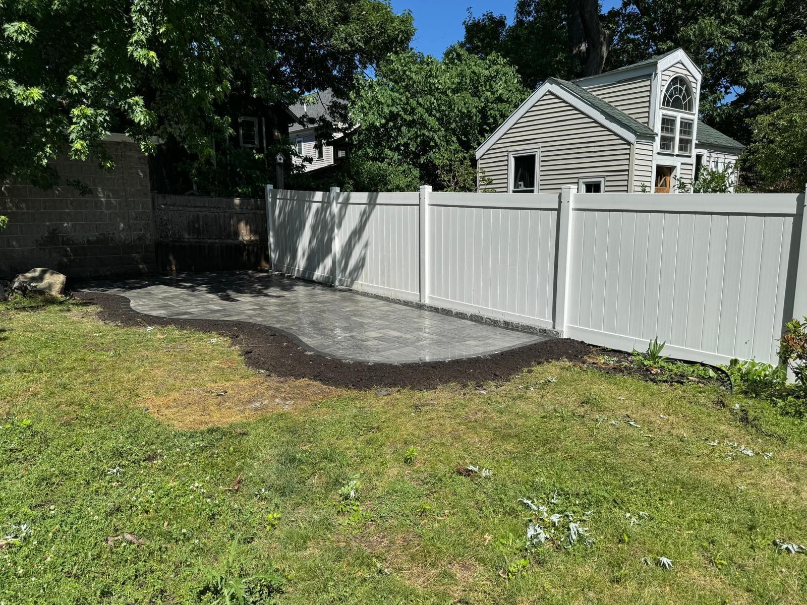 Backyard with white vinyl fence, gravel patio, and green grass.