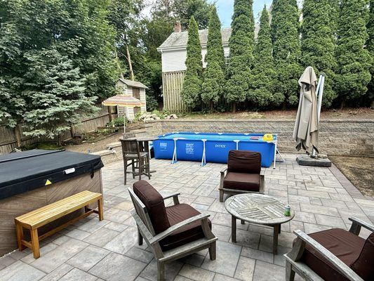 Backyard patio with hot tub, chairs, small pool, and trees.