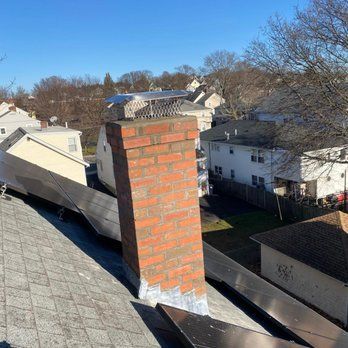 Brick chimney on a roof with asphalt shingles. The chimney appears to be leaning slightly. In a residential area.