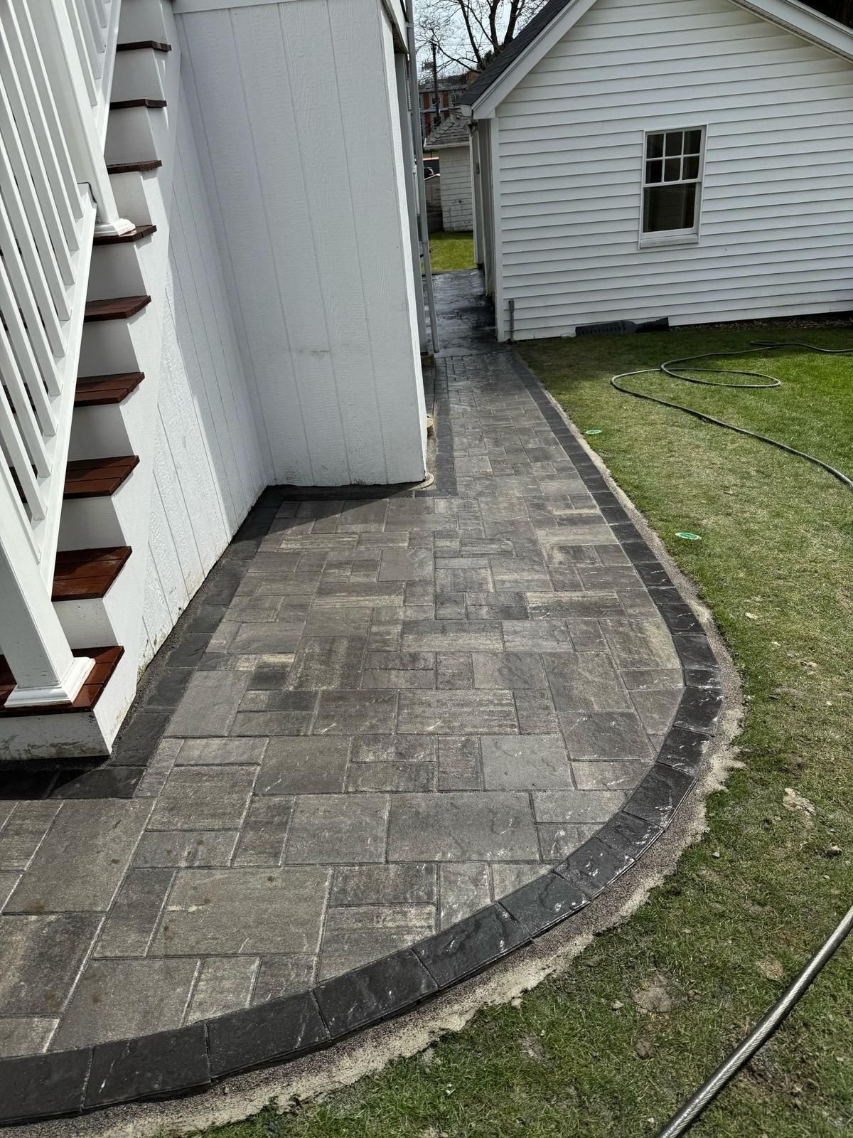 Brick walkway next to white wall and stairs, leading towards a white building and grass.