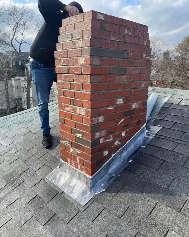 Person on a roof repairing a brick chimney with silver flashing.