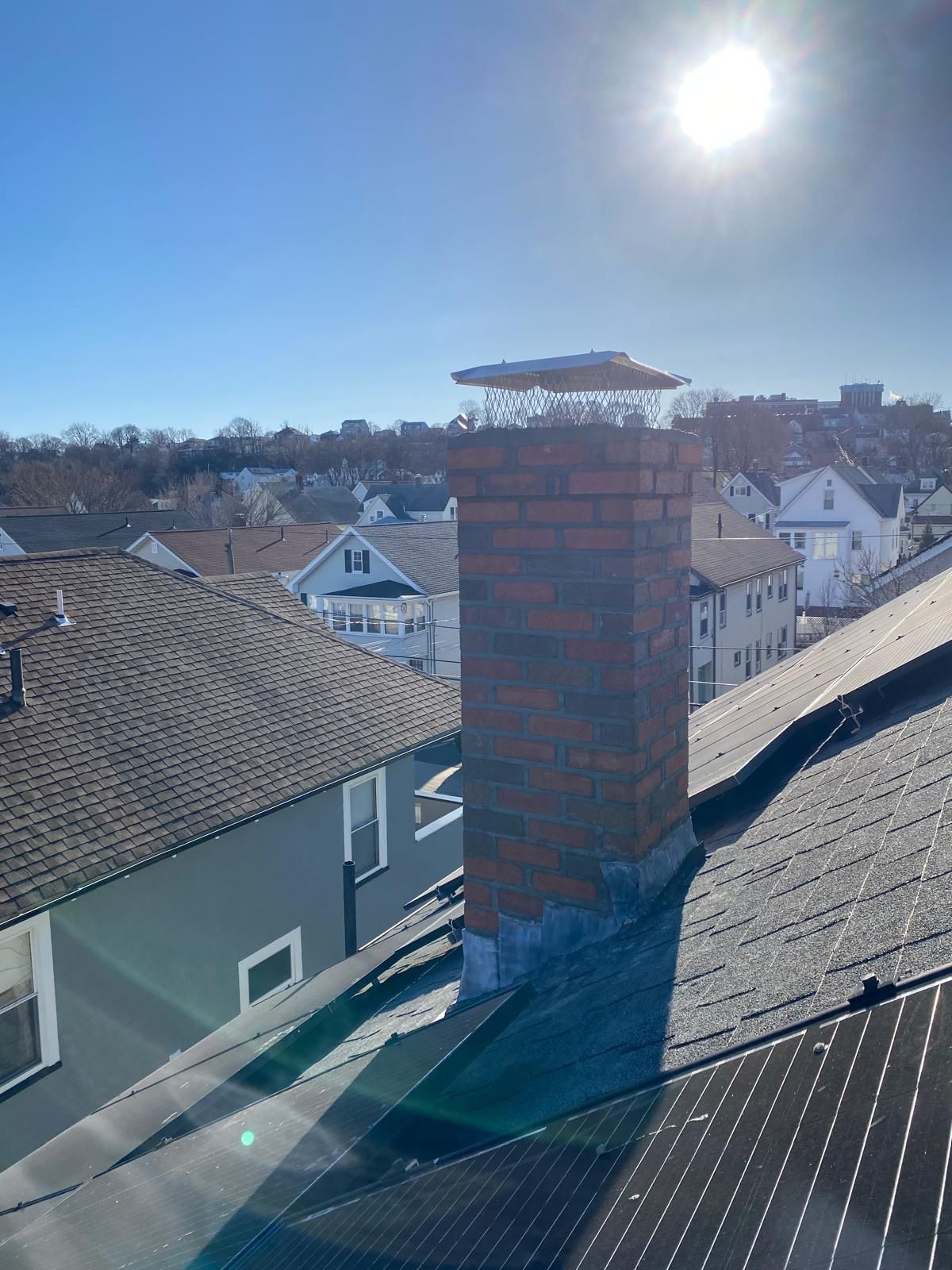 Brick chimney on a rooftop with clear skies and sunlight. Buildings in background.
