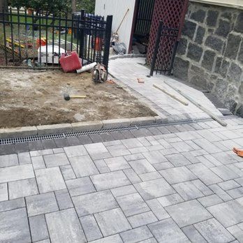 Paver patio construction with installed drain and stone retaining wall.
