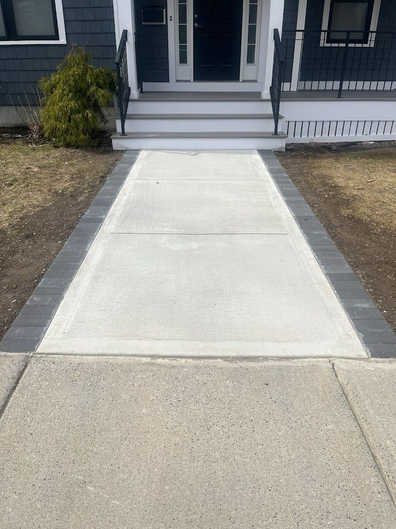 Concrete walkway leading to house entrance with gray stone borders.