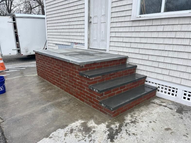Brick steps leading to a door; white shingled building.