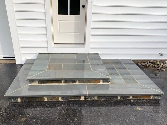 Gray stone steps leading to a white door. The steps are rectangular with a stone border.