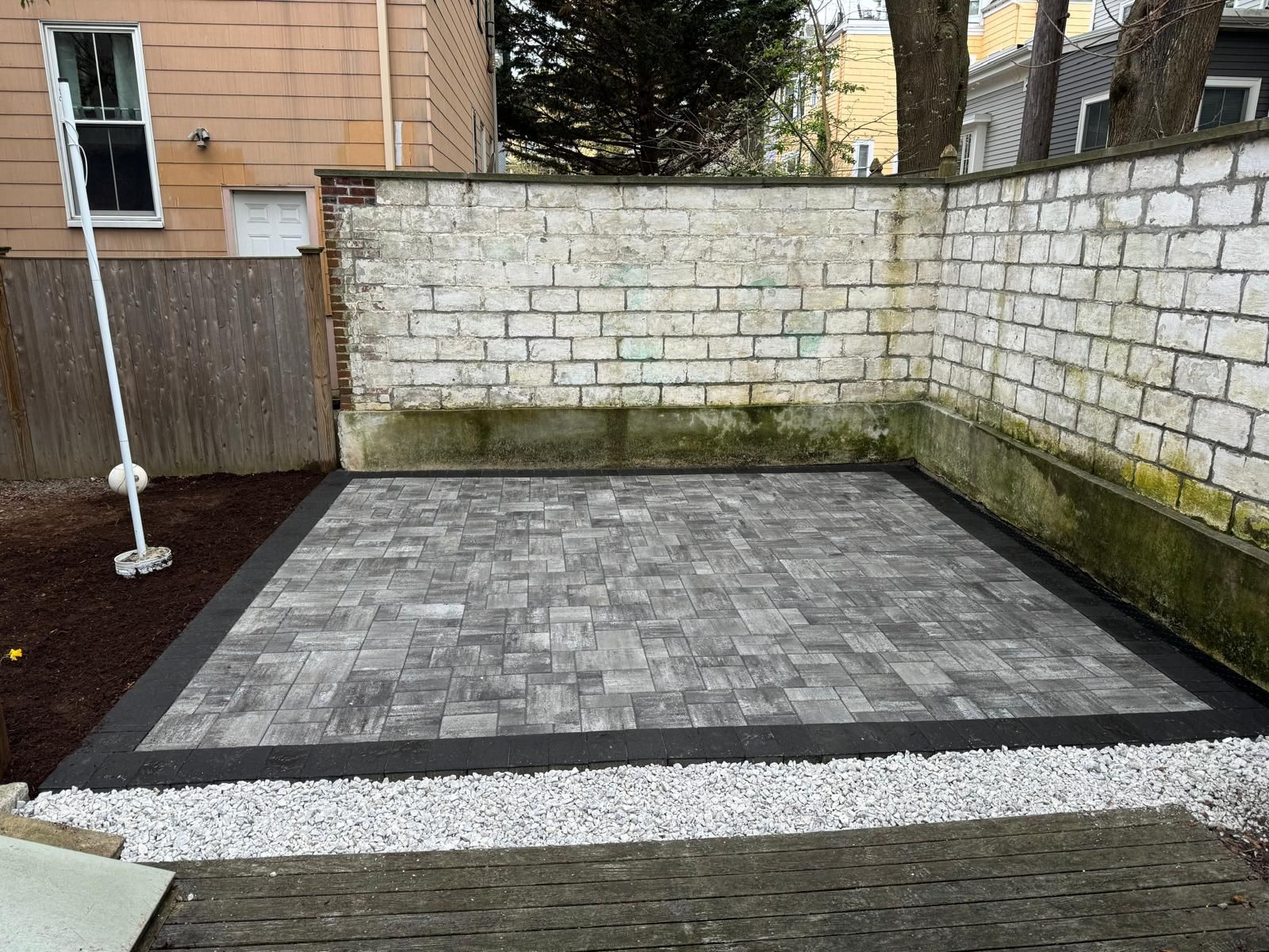Paver patio surrounded by white gravel, black border, and brick walls.