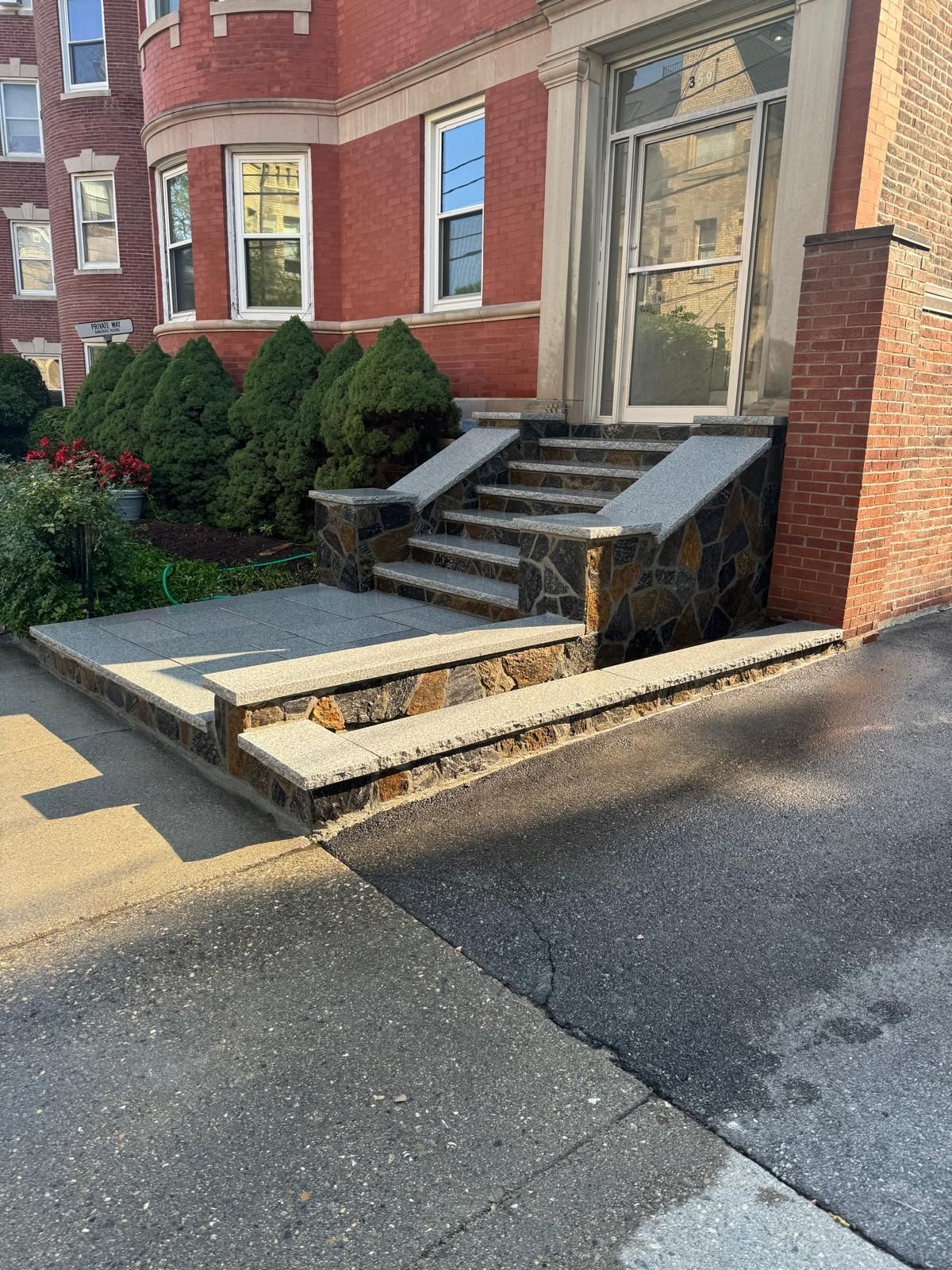 Brick building entrance with stone steps, a sidewalk, and asphalt.
