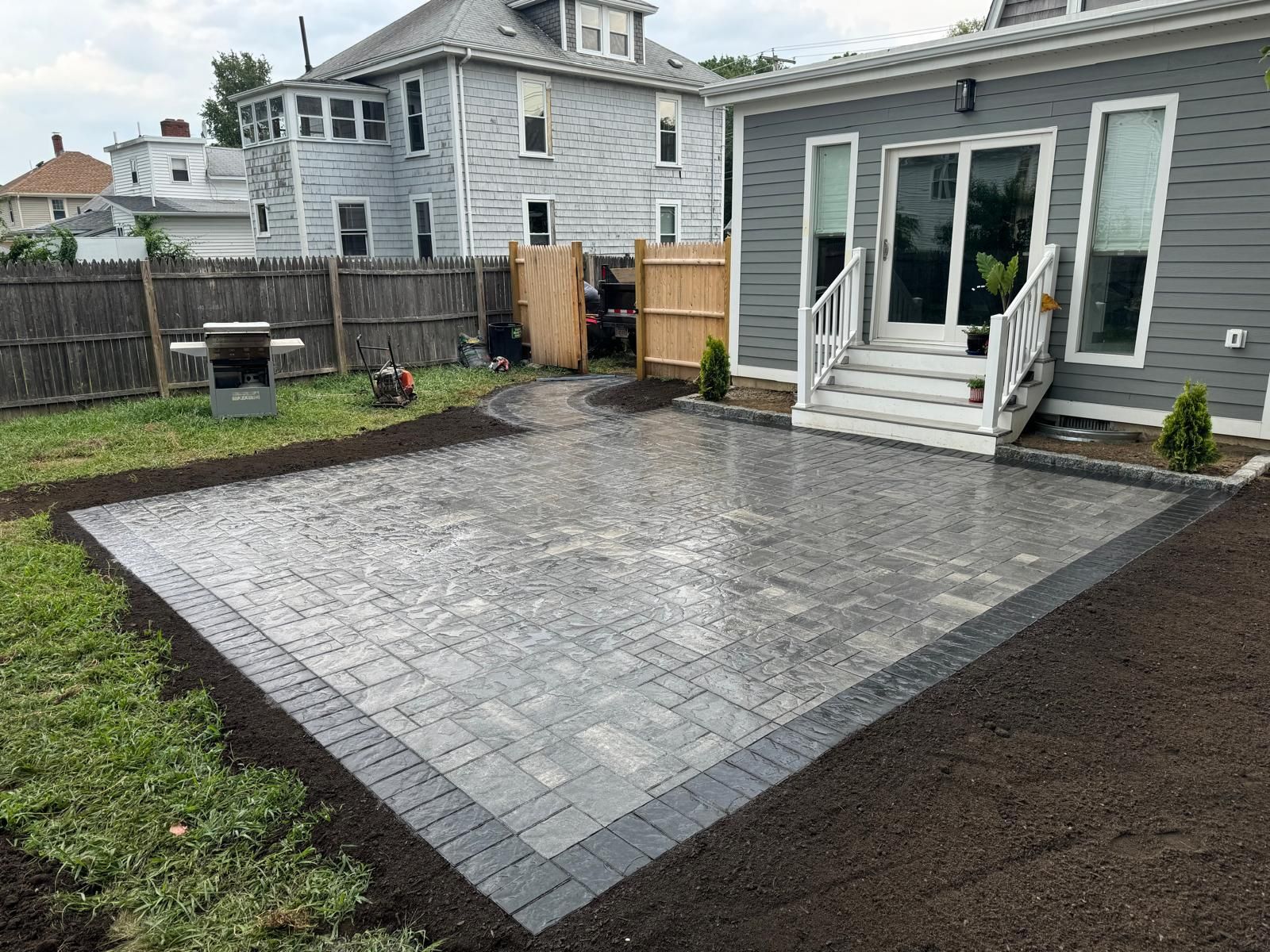 Backyard patio with gray brick pavers, dark border, and sliding glass door.