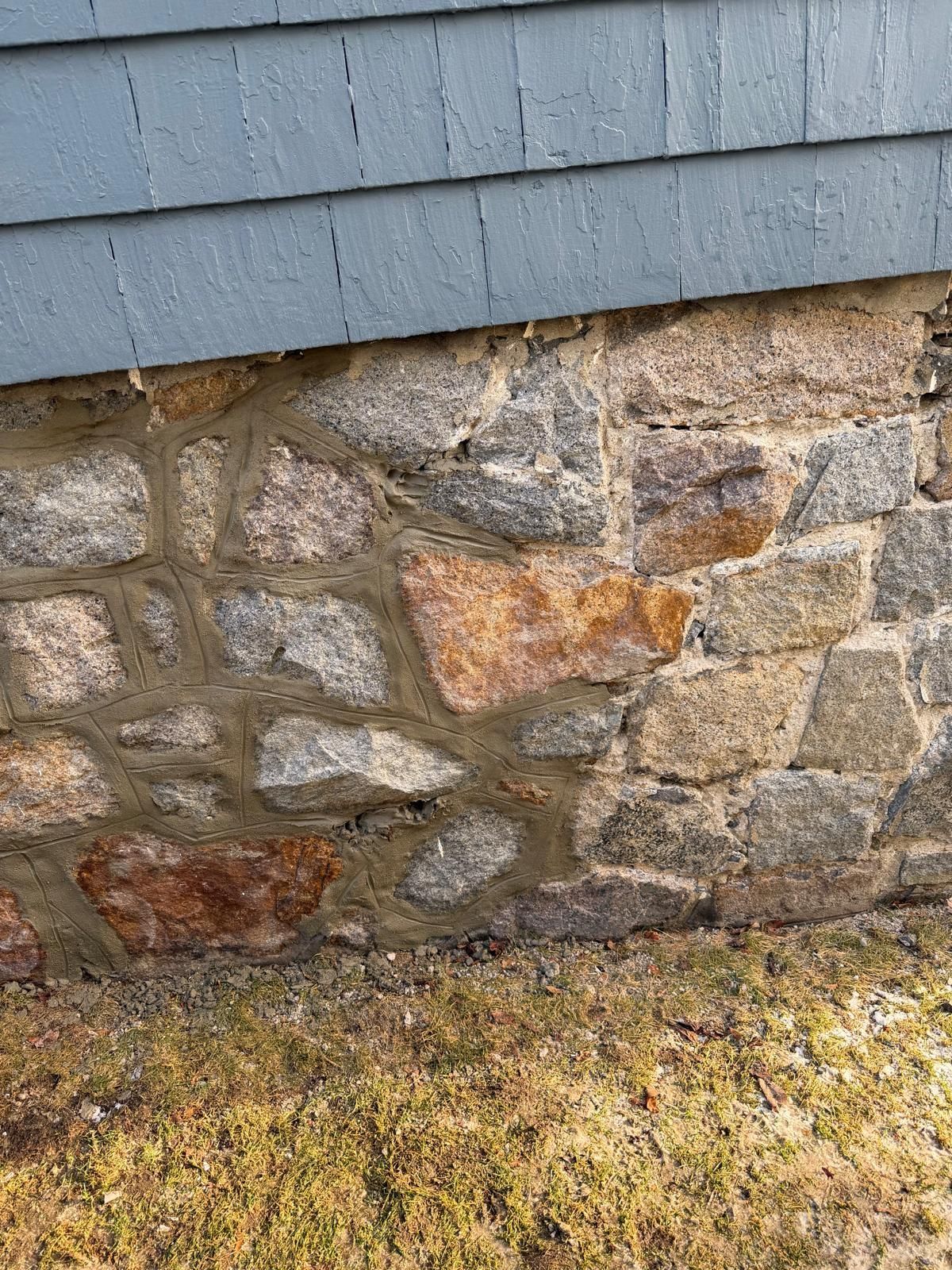 Stone foundation of a building with blue siding above it, set in brown grass.